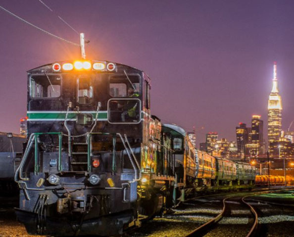 New York & Atlantic Railway train at night with the NY skyline in the background.